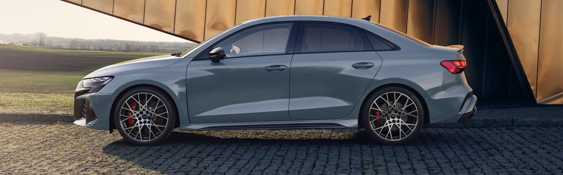 Audi RS 3 Limuzína zaparkované na dlažobných kockách, v pozadí vidieť modernú budovu.