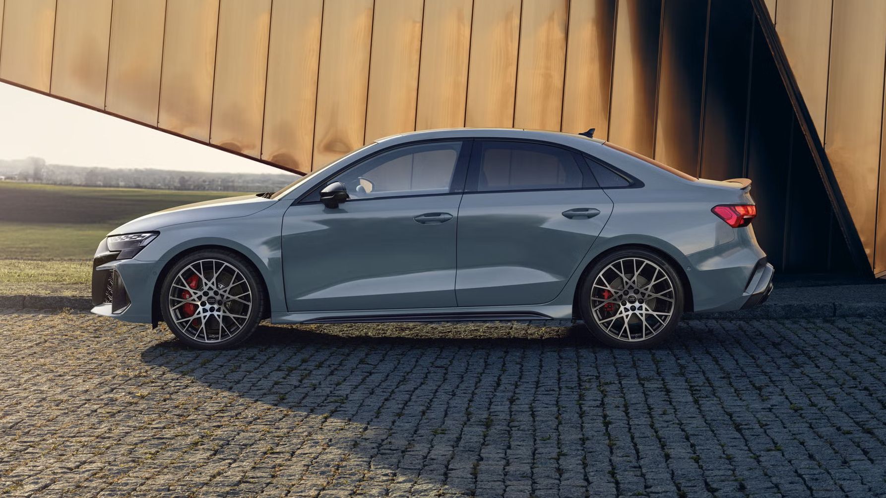 Audi RS 3 Limuzína zaparkované na dlažobných kockách, v pozadí vidieť modernú budovu.