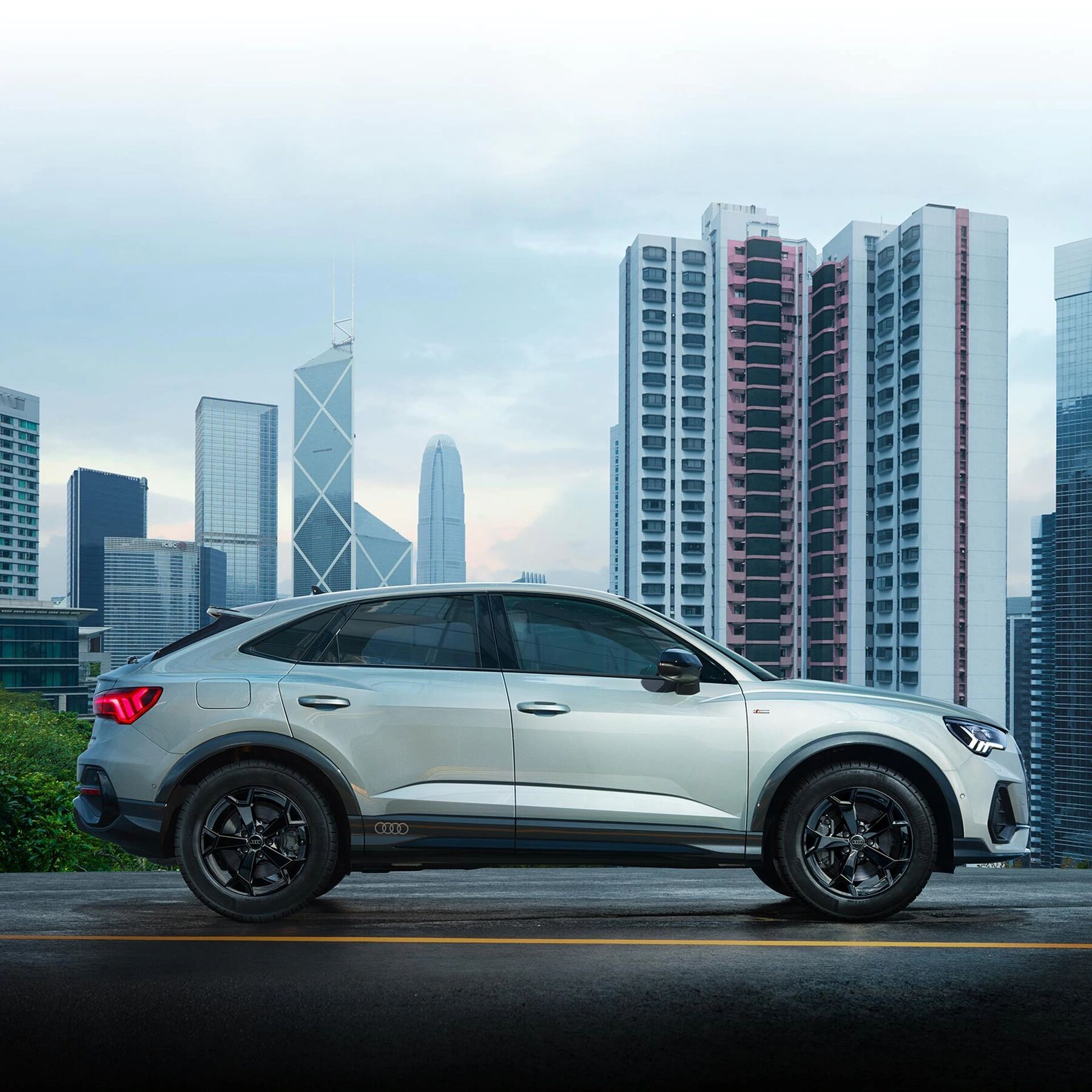 Audi Q3 z bočného pohľadu, za vozidlom vidieť výškové budovy.