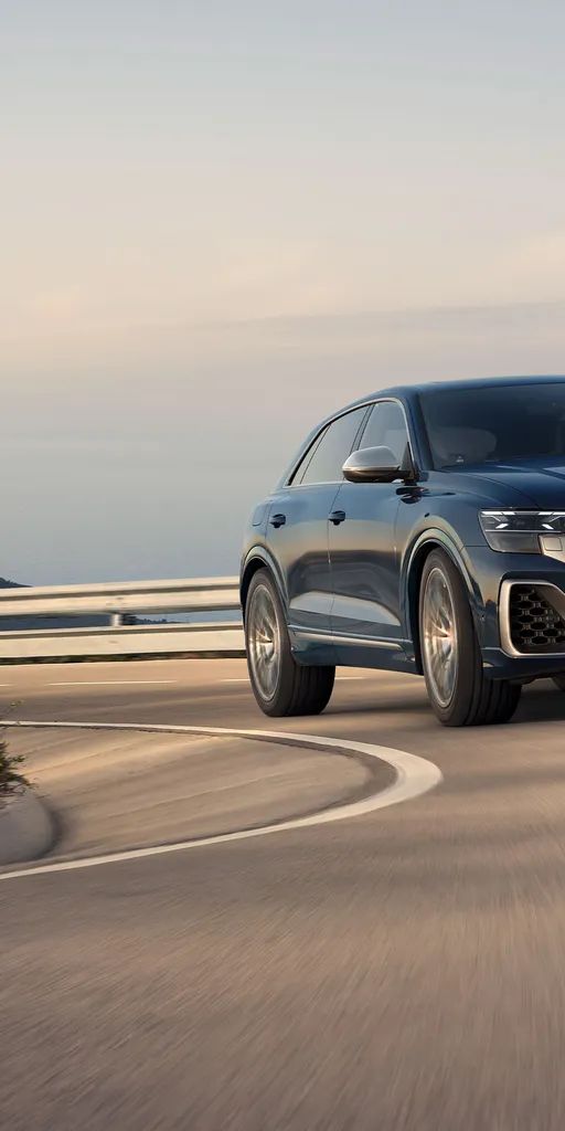 Audi SQ8 SUV jazdí po ceste v zákrute. V pozadí je výhľad na široké more.
