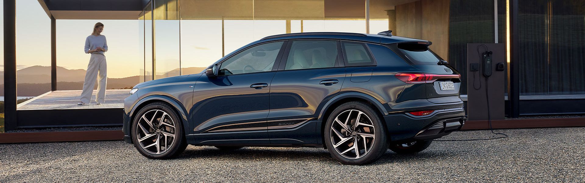 Audi Q6 SUV e-tron z bočného pohľadu pri modernom dome.