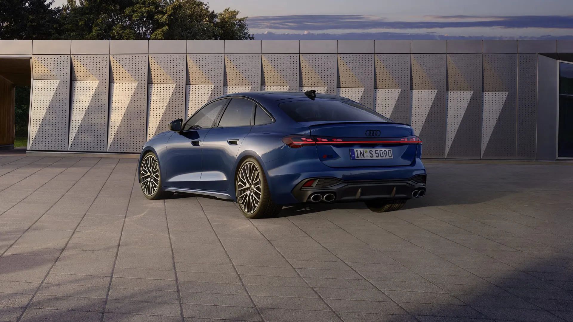 Audi S5 Limuzína in dunkelblau stojí šikmo pred fasádou budovy a je osvetlený slnečným svetlom.