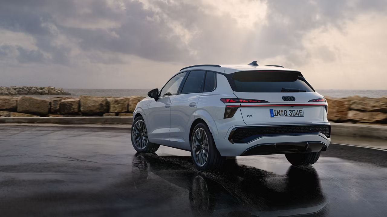 Biele Audi Q3 SUV e-hybrid zaparkované na parkovisku pri pobreží.