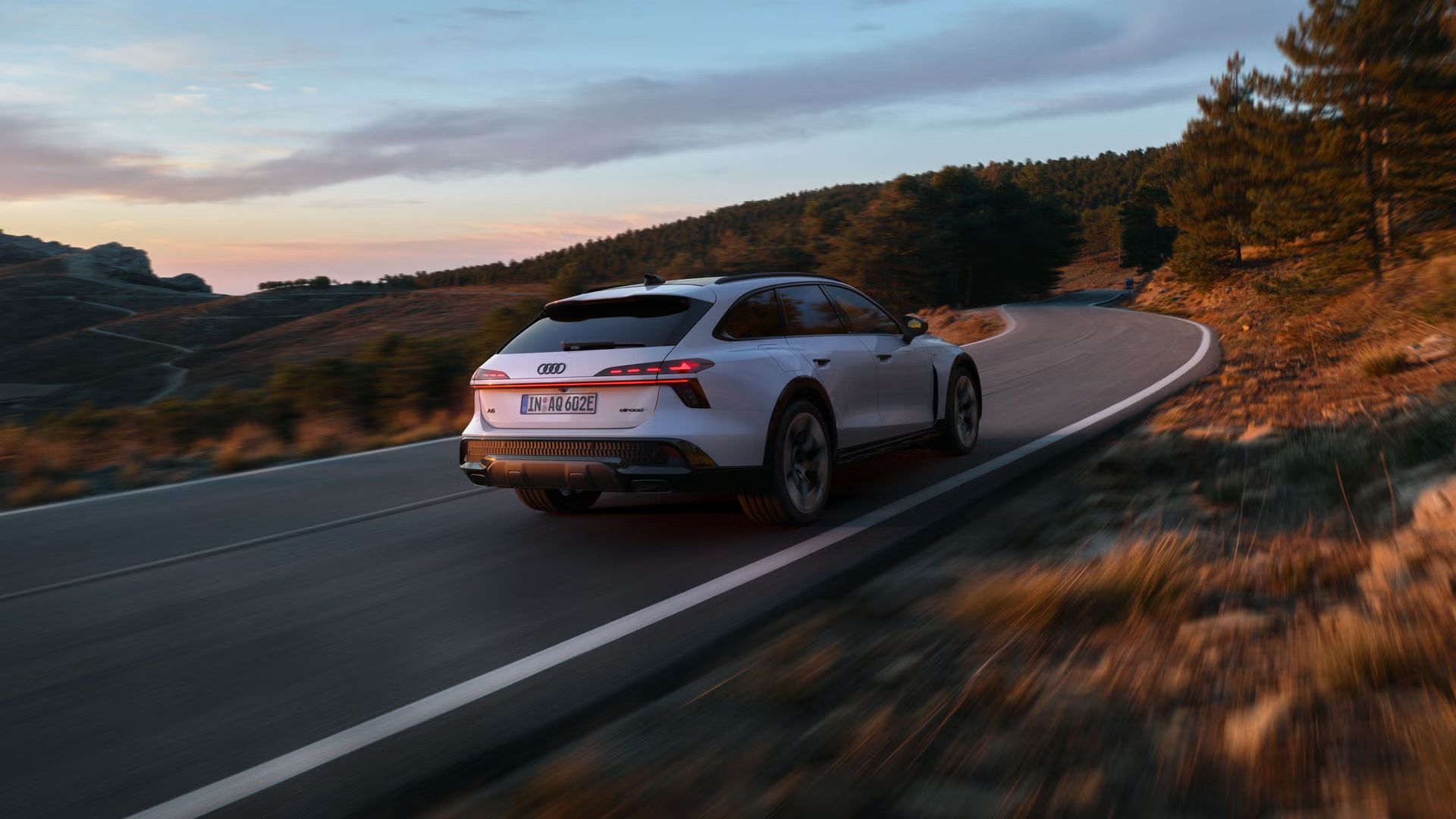 Audi A6 allroad e-hybrid zachytené z bočného pohľadu zo zadnej strany pri plnej rýchlosti na horskej ceste. V pozadí je les.