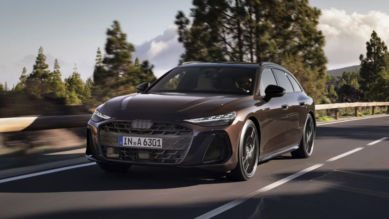 Audi A6 Avant počas jazdy na ceste. Cestu lemujú zvodidlá, zeleň a ihličnaté stromy. Nebo je čiastočne zatiahnuté.