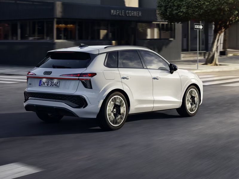 Biele Audi Q3 SUV e-hybrid zozadu vpravo počas jazdy na križovatke v centre mesta.