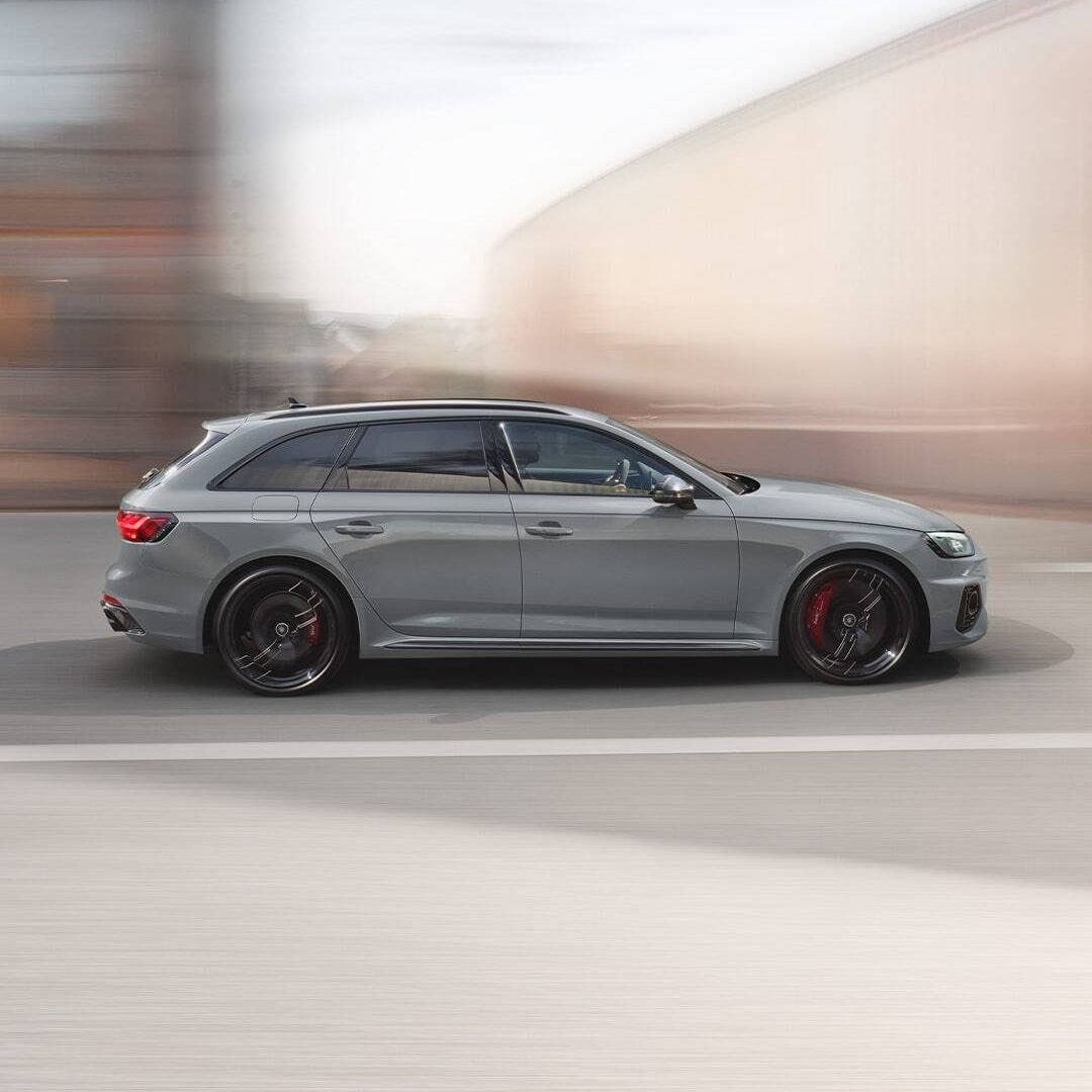 Športové, strieborné Audi RS 4 Avant v pohybe na ceste. Pozadie je rozmazané, čo zdôrazňuje rýchlosť vozidla. Auto má čierne ráfiky a červené brzdové strmene.