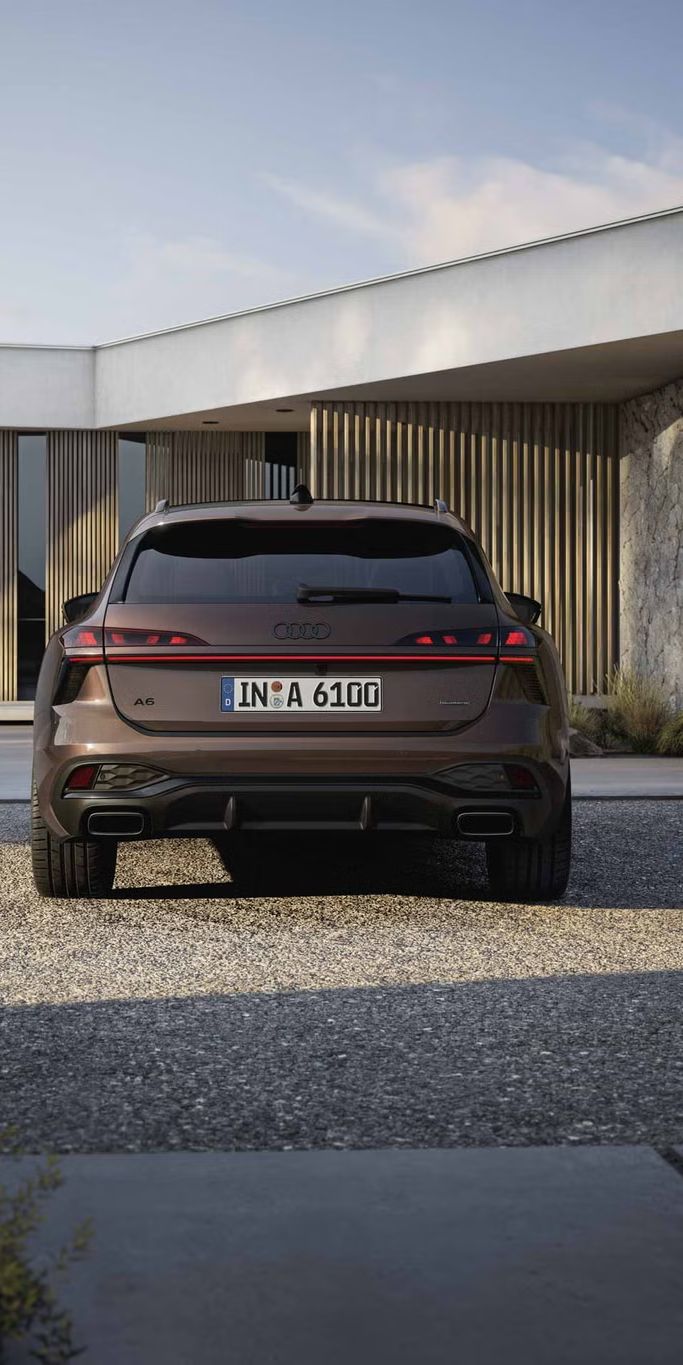 Heckaufnahme des A6 Avant, der auf einer Kiesfläche vor einer Fassade mit Holzvertäfelung und hohen Fenstern steht.