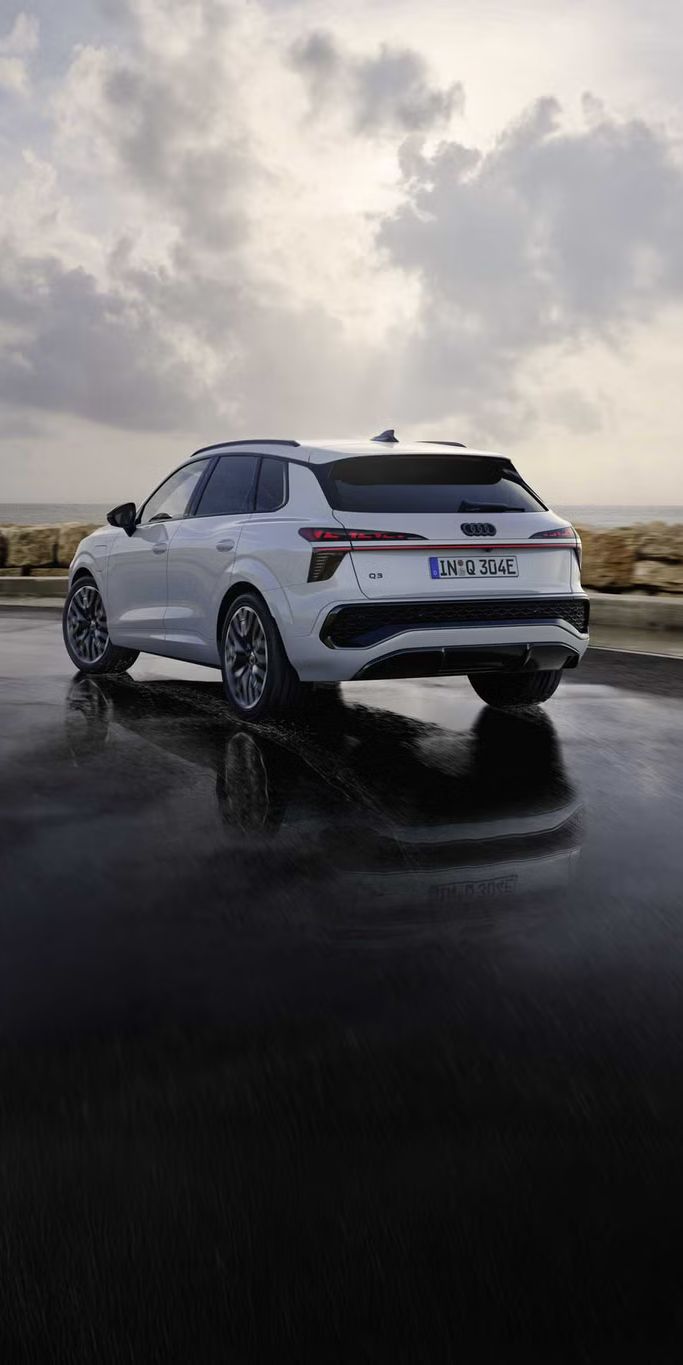 Biele SUV Q3 e-hybrid jazdí po mokrej ceste pozdĺž pobrežia.