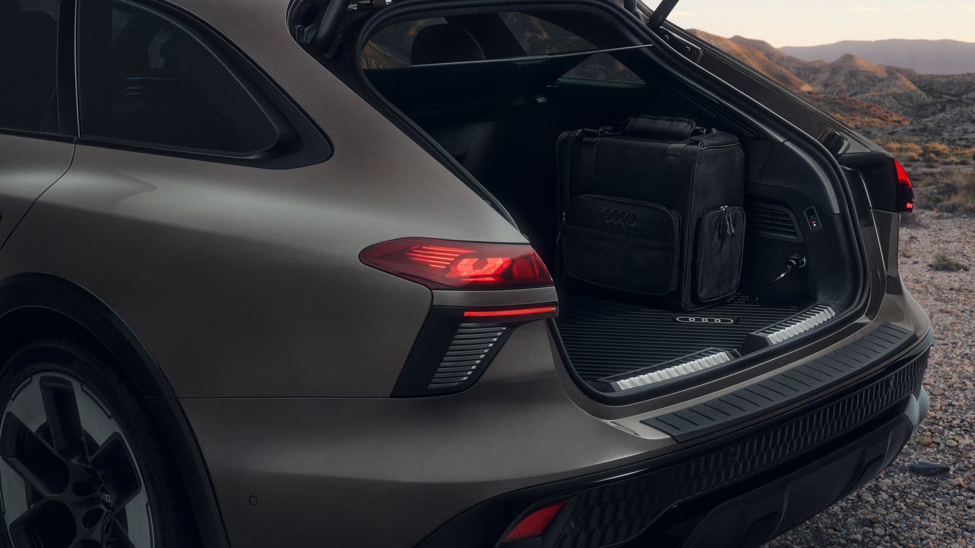 Záber zblízka na zadnú časť vozidla Audi A6 allroad, ktoré parkuje na štrkovej ceste. V otvorenom batožinovom priestore stojí 14-litrová chladiaca taška.