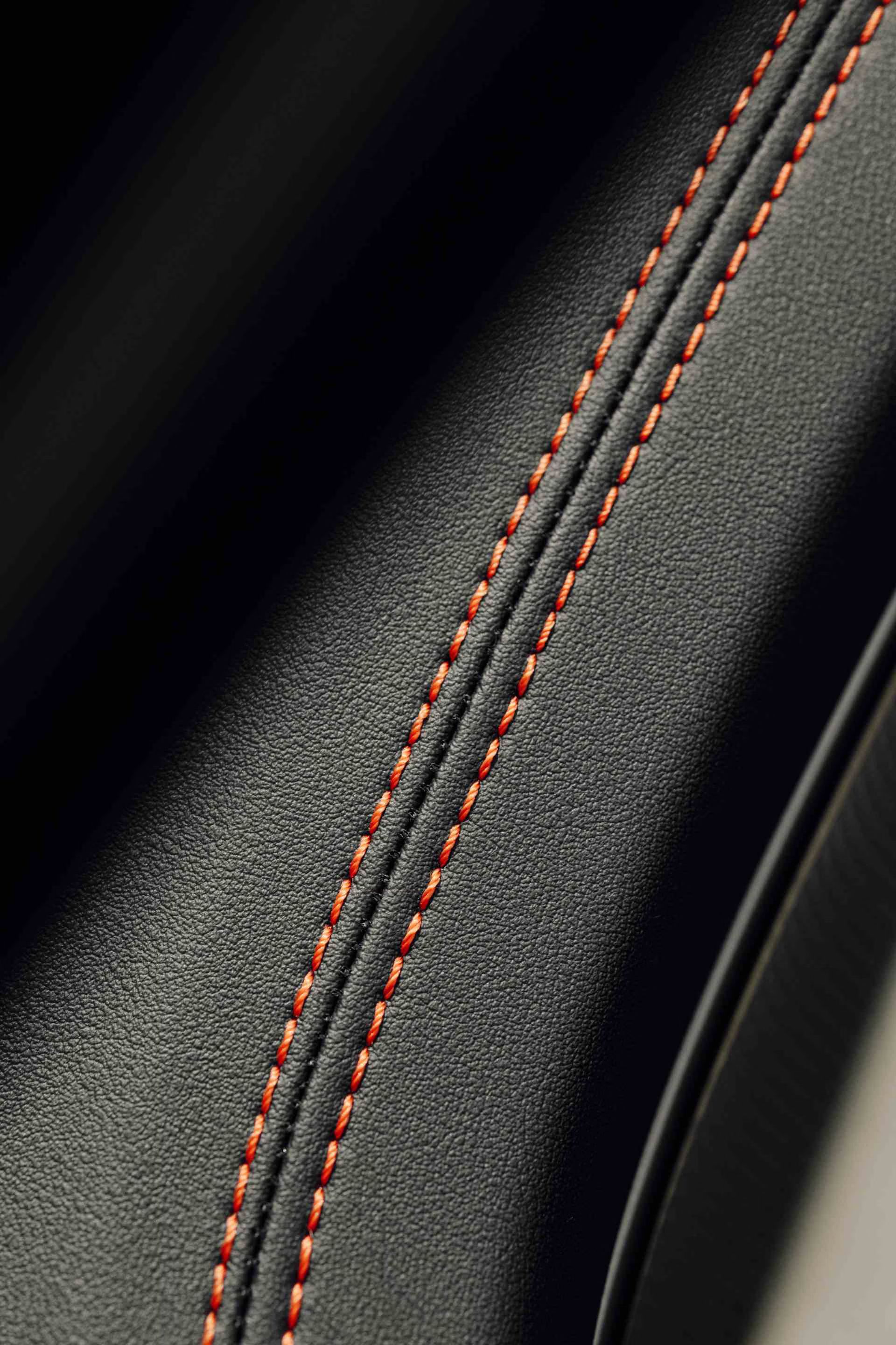 Detail na čiernu kožu sedadla s oranžovými švami.
