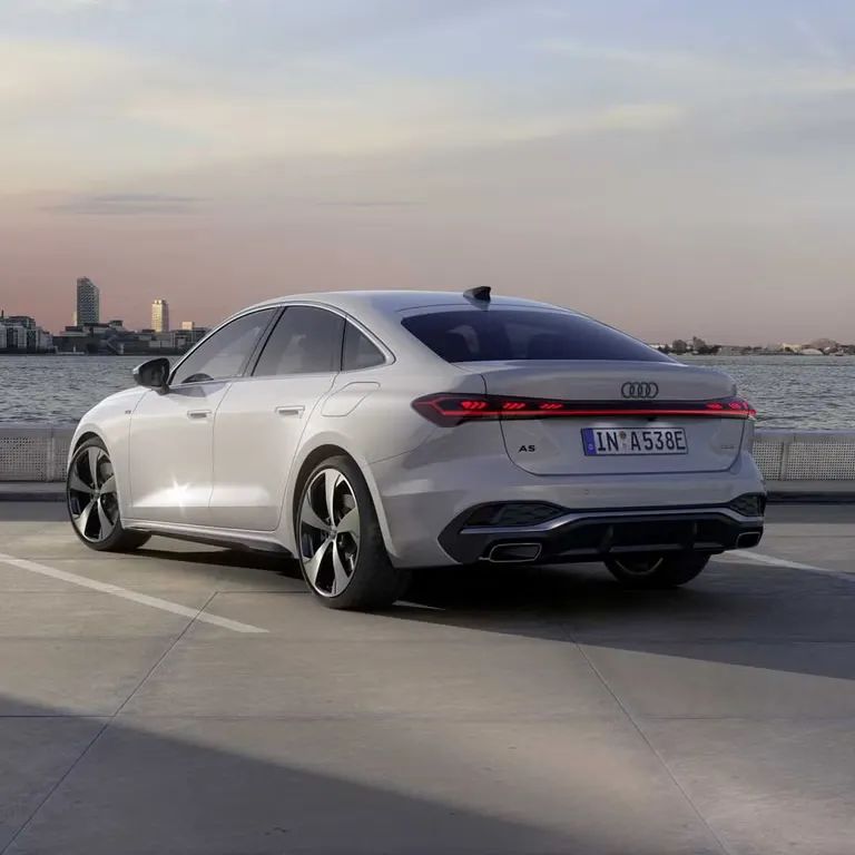 Audi A5 Limuzína e-hybrid je zaparkovaná na parkovisku na móle pri mori. V pozadí je panoráma meste.