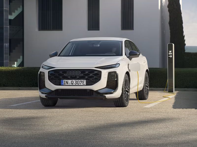 Audi Q3 Sportback e-hybrid zaparkovaný pre moderným, bielym bytovým domom pri verejnej nabíjacej stanici. Vozidlo sa nabíja.
