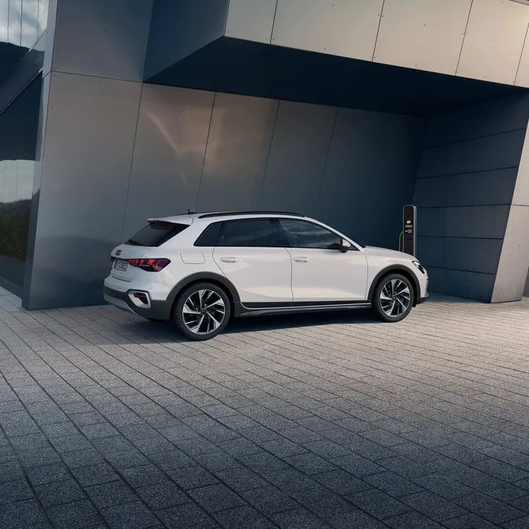 Audi A3 allstreet TFSI e zapojené k nabíjacej verejnej stanici pri modernej budove a nabíja sa.