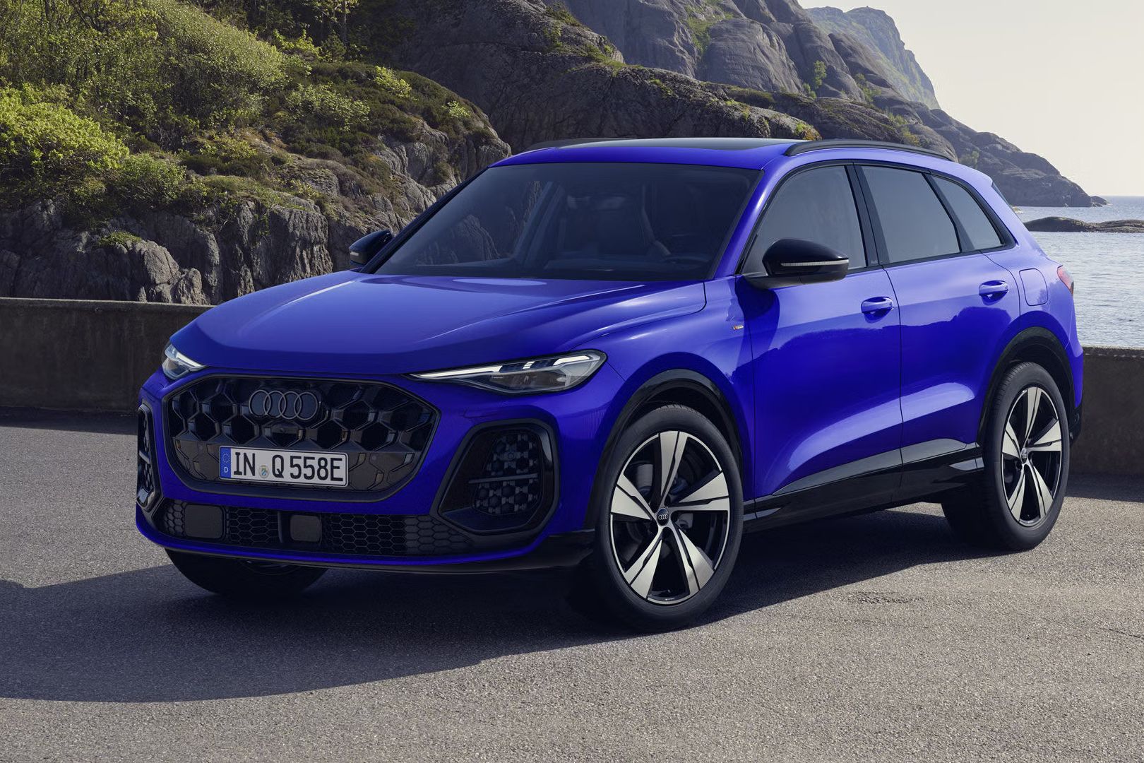 Modré Q5 SUV e-hybrid s individuálnym lakovaním v modrom odtieni Nogaro s perleťovým efektom stojí v šikmom prednom profile na pobreží.