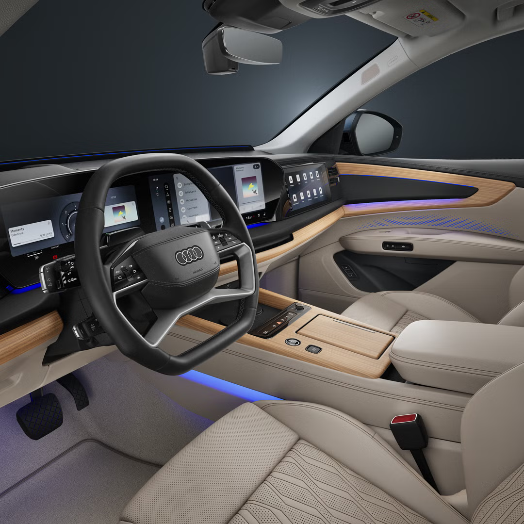 Pohľad do kokpitu Audi Q7 SUV s čiernym volantom, dotykovou obrazovkou, koženým čalúnením a modrým interakčným osvetlením.