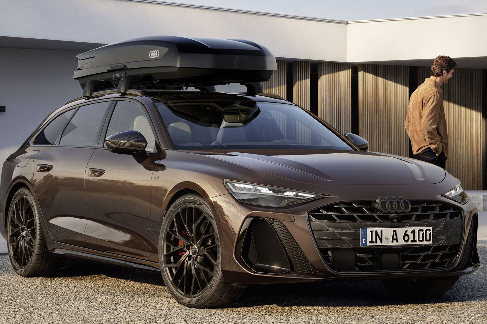 A6 Avant stojí pred moderným domom. Na streche je strešný box s logom Audi. Vľavo od vozidla stojí muž.