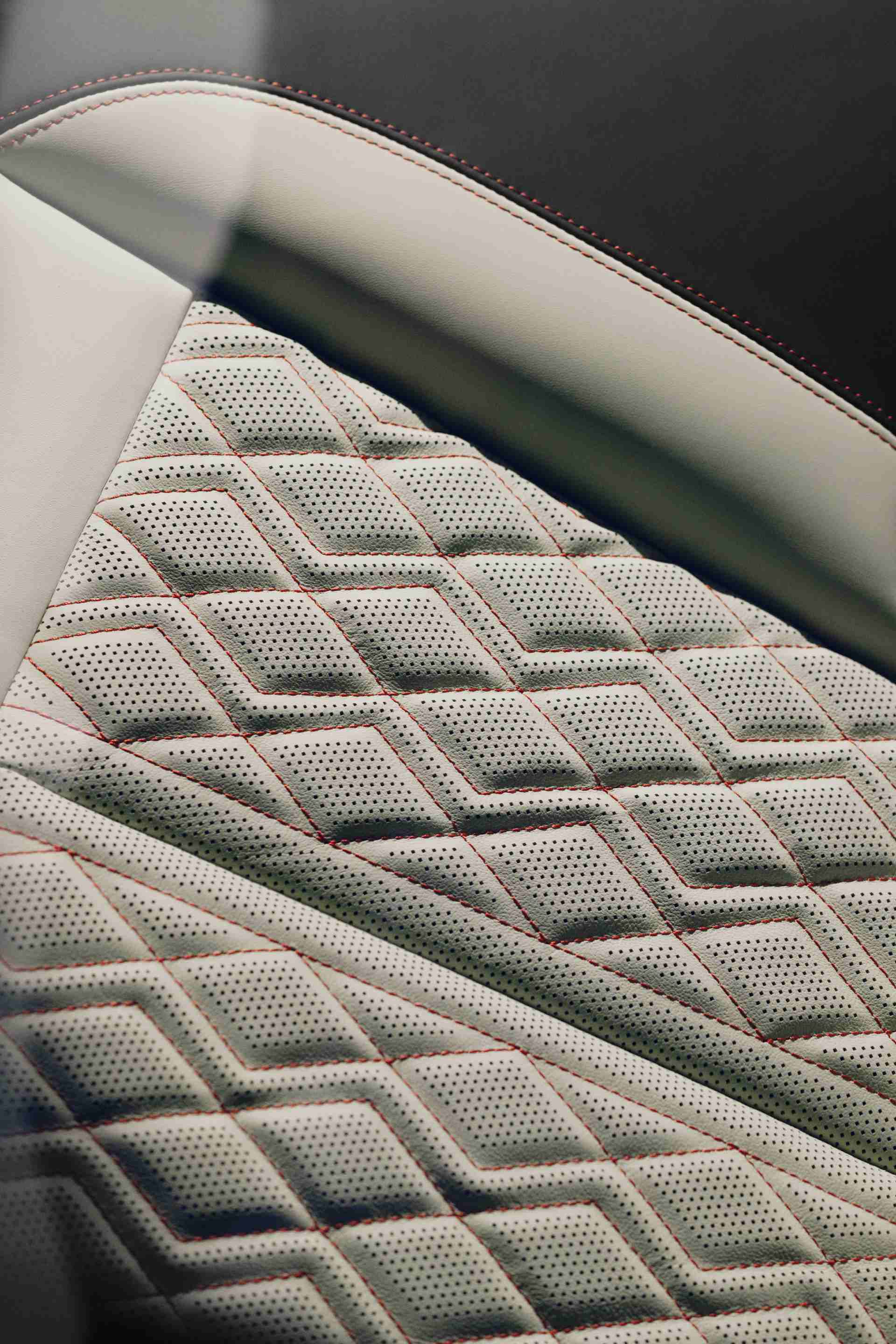 Detailný záber na luxusné vzorované kožené čalúnenie automobilového sedadla. Čalúnenie je perforované a má geometrický vzor. Farby sú svetložlté s s farebnými stehmi..