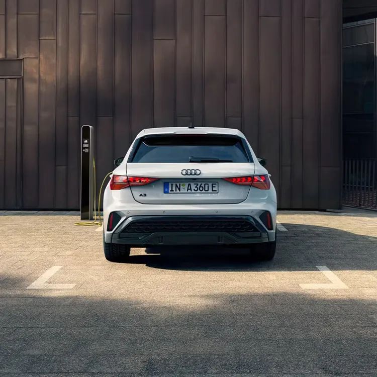 Audi A3 Sportback TFSI e zaparkovaný na parkovacom mieste pred budovou a pri nabíjacej stanici. Pohľad na zadné partie vozidla.