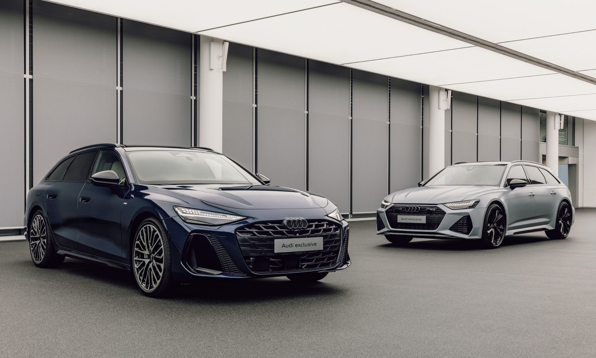 Dva moderné Audi automobily zaparkované vedľa seba v interiéri. Jedno auto je tmavomodré a druhé je sivé.