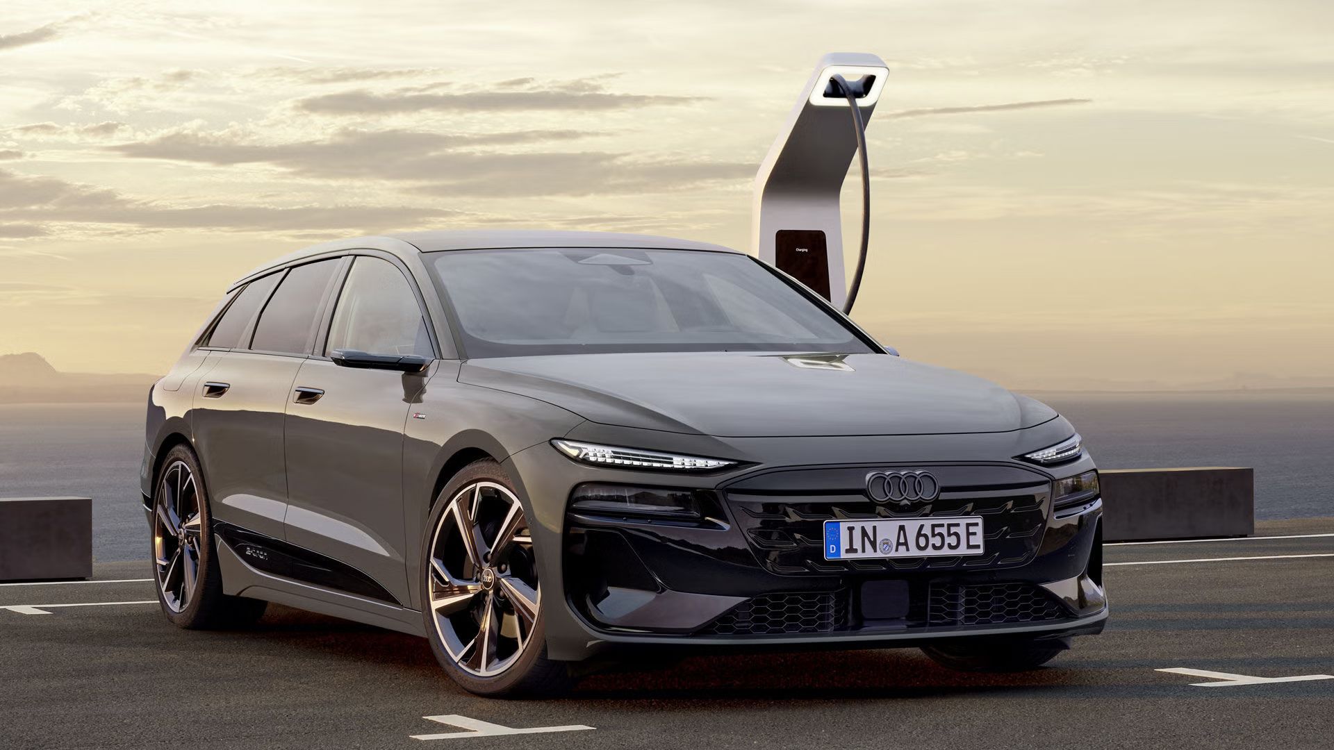 A6 Avant e-tron stojí v zadnej časti parkoviska a je pripojený k nabíjacej stanici. V pozadí je vidieť more a hory. 