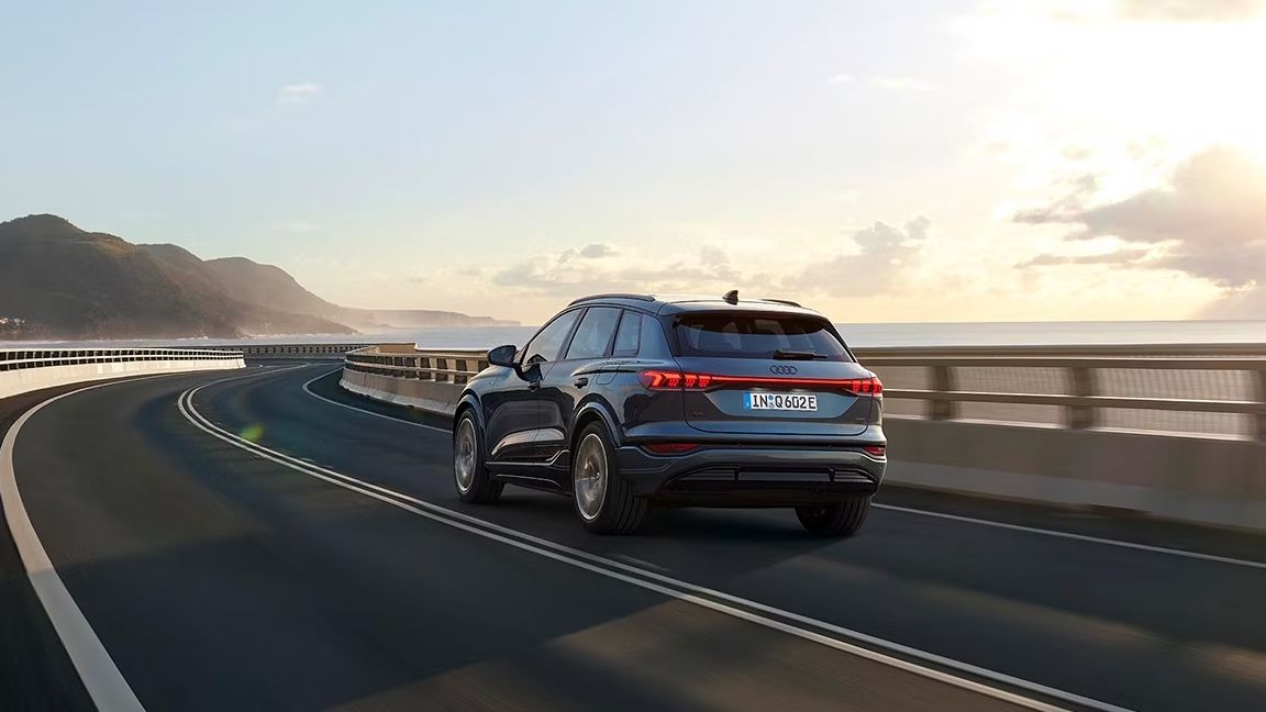 Pohľad na zadné partie Audi Q6 počas dynamickej jazdy po ceste popri pobreží.