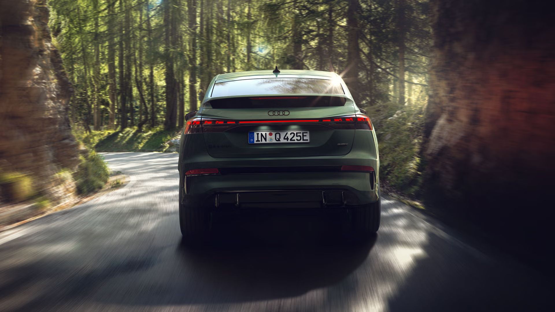 Q4 Sportback e-tron zozadu pri jazde lesom, po ľavej i pravej strane cesty sa týčia skaly.