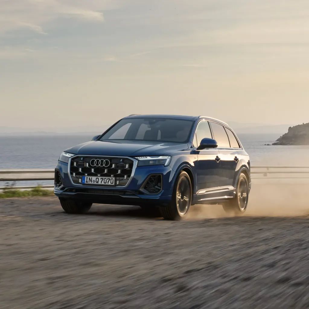 Audi Q7 SUV jazdí po ceste popri pobreží.