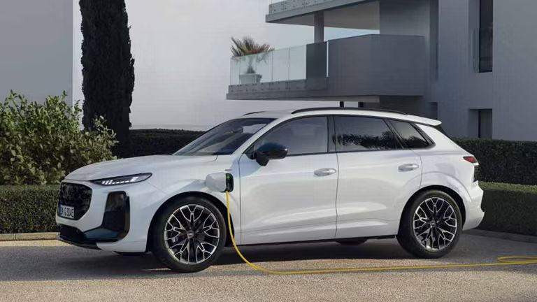 Biele Audi Q3 SUV e-hybrid stojí pre moderným bytovým domom, ktoré sa nabíja.