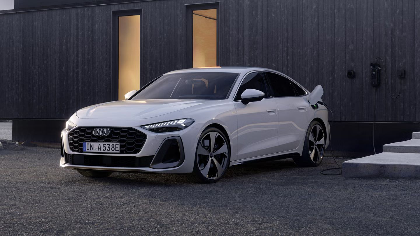 Pohľad na predné partie Audi A5 Limuzína e-hybrid. Vozidlo stojí pred tmavou fasádou budovy a je pripojené k nabíjacej stanici.
