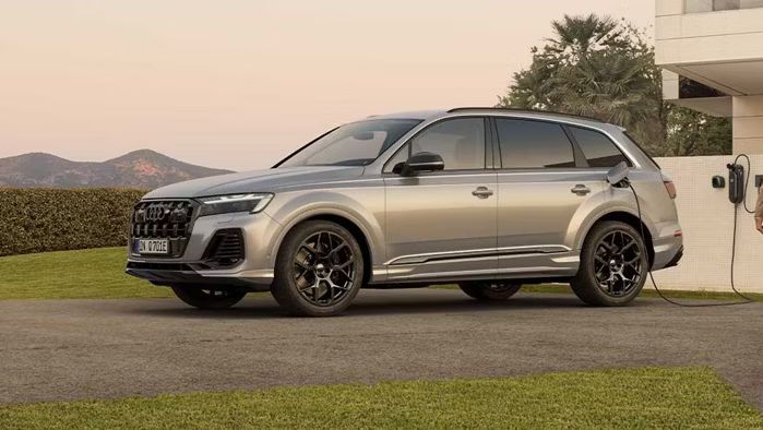 Bočný pohľad na strieborné Audi Q7 SUV TFSI e pri nabíjaní pred modernou vilou. 