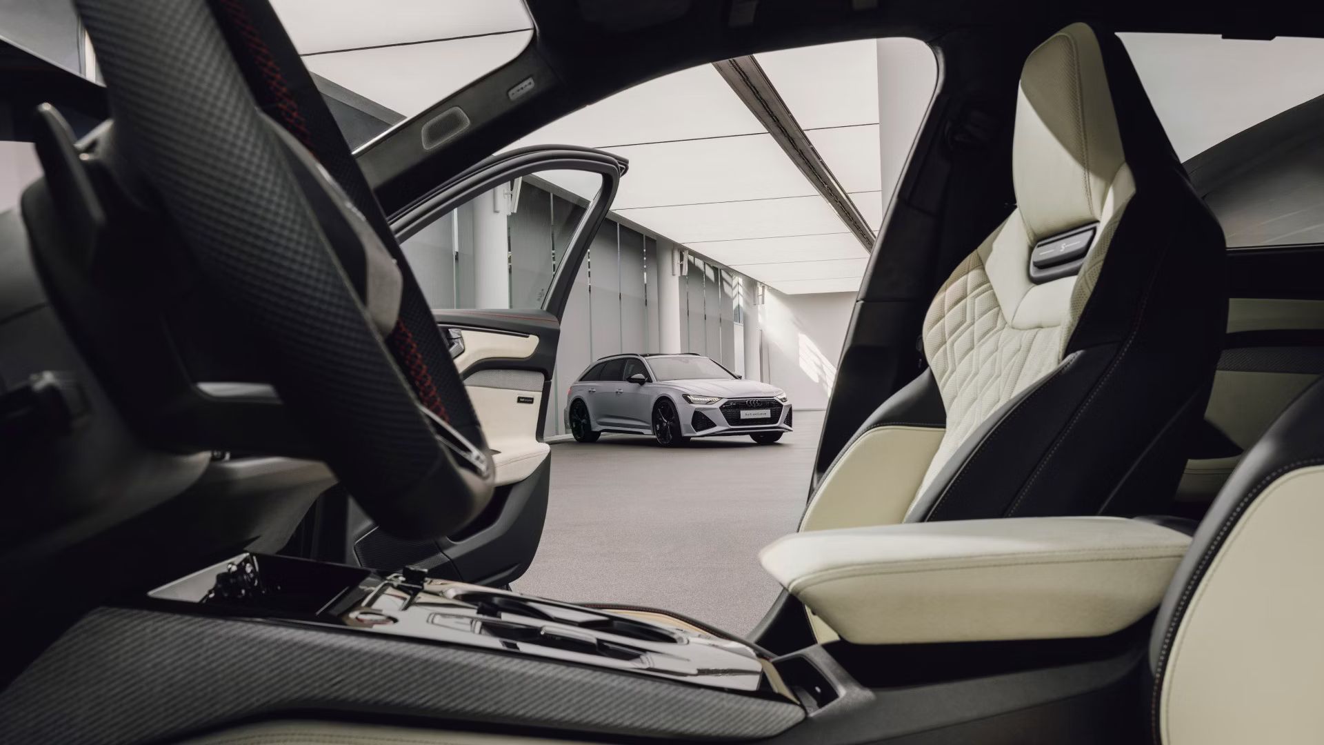 Pohľad na Audi A6  Avant zaparkovaný pri bielej, modernej, industriálnej budova z pohľadu interiéru prémiového Audi s koženou výbavou.