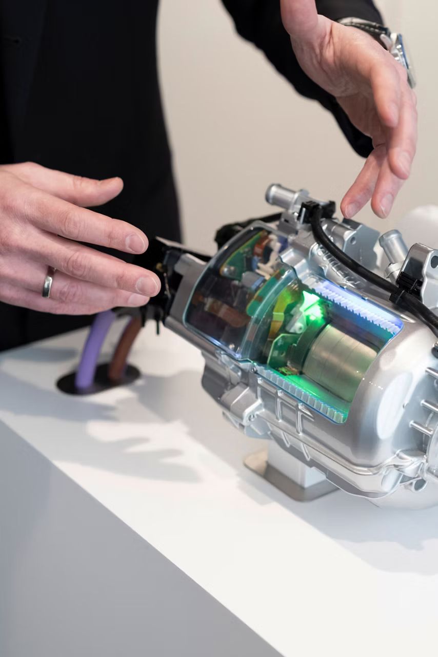 Detailný pohľad na hnací modul, ktorý je umiestnený na bielom podstavci. Pri podstavci stojí človek a vidieť jeho ruky.