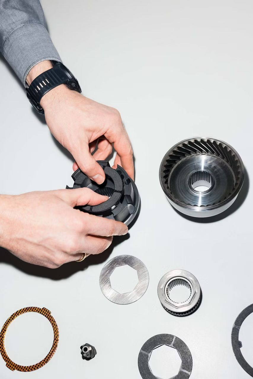 Pohľad na ruky, ktoré držia súčiastku. Okolo nich sú na stole rozložené ďalšie súčiastky.