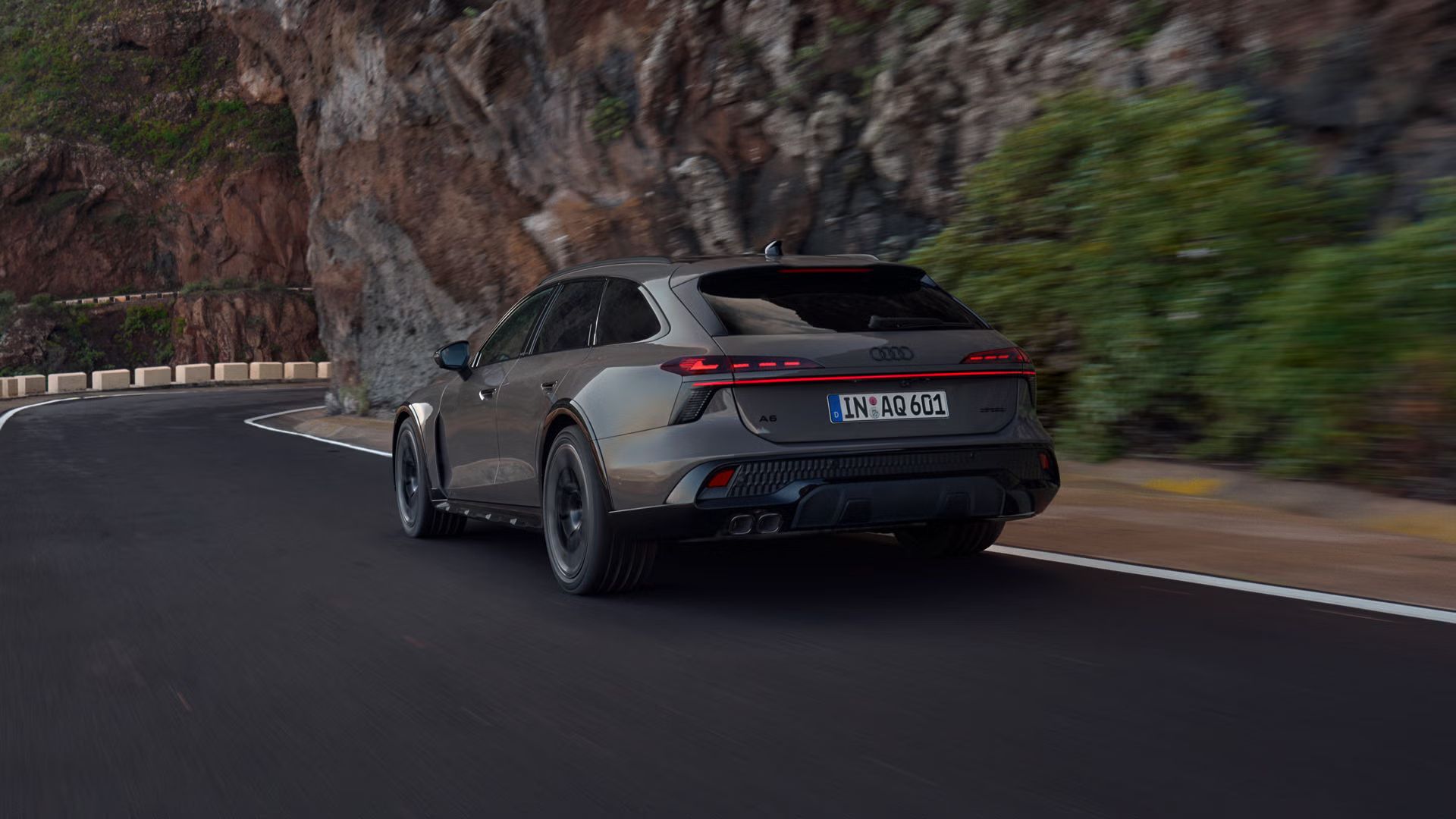 Audi A6 allroad v šikmom pohľade zozadu pri plnej rýchlosti na horskej ceste. Vpravo sa týčia strmé skalné steny.