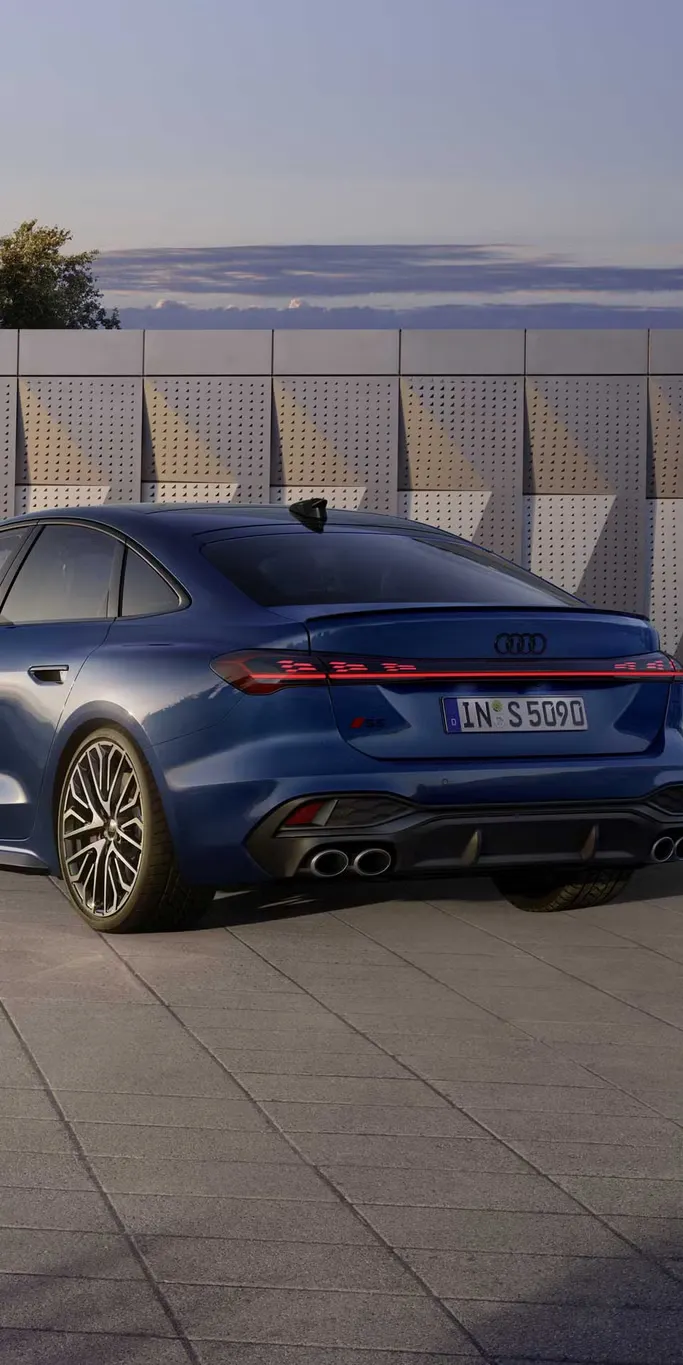 Die S5 Limousine in dunkelblau steht schräg vor einer Gebäudefassade und wird dabei vom Sonnenlicht angestrahlt.