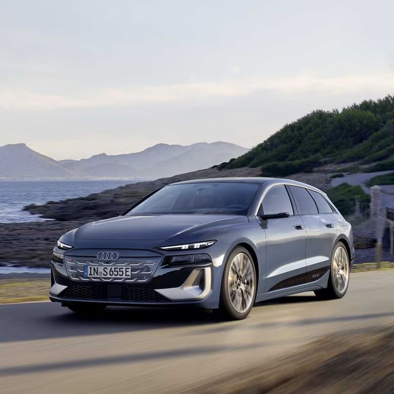 S6 Avant e-tron z bočného pohľadu spredu prechádza po ceste pozdĺž pobrežia. V pozadí sú vidieť kopce. 