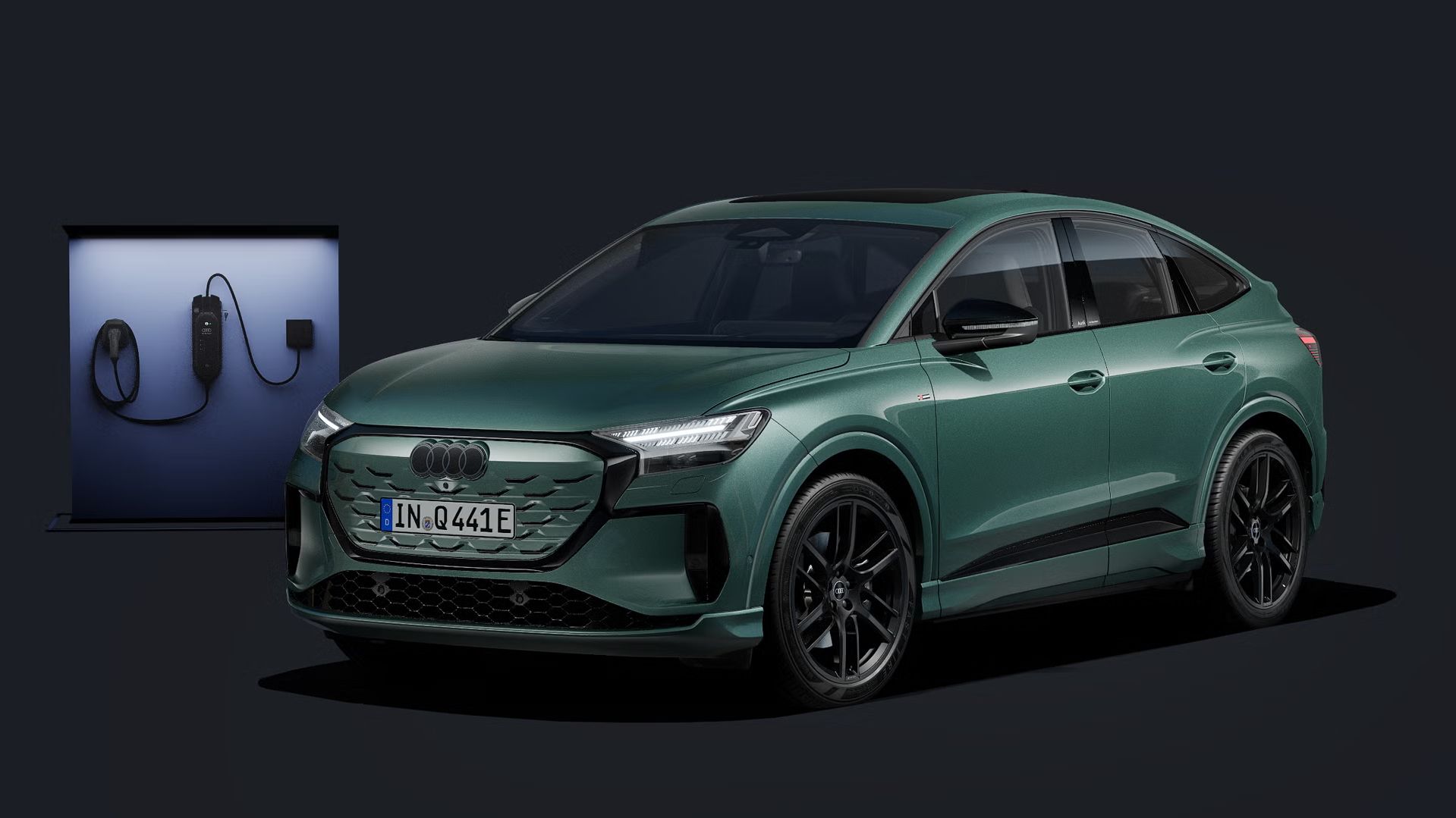 Q4 Sportback e-tron zobrazený z čelného pohľadu na tmavom pozadí, za ním moderná nabíjacie stanica.