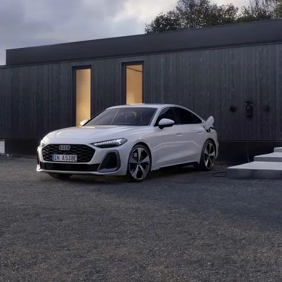 Audi A5 Limuzína e-hybrid zaparkované pri modernom, drevenom dome je napojené na nabíjaciu stanicu a nabíja sa.