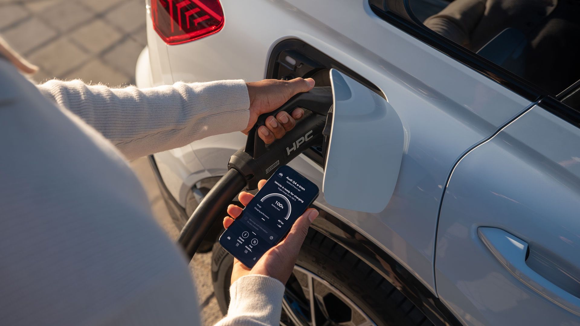 Osoba nabíja elektromobil pri nabíjacej stanici a sleduje priebeh nabíjania prostredníctvom aplikácie MyAudi.