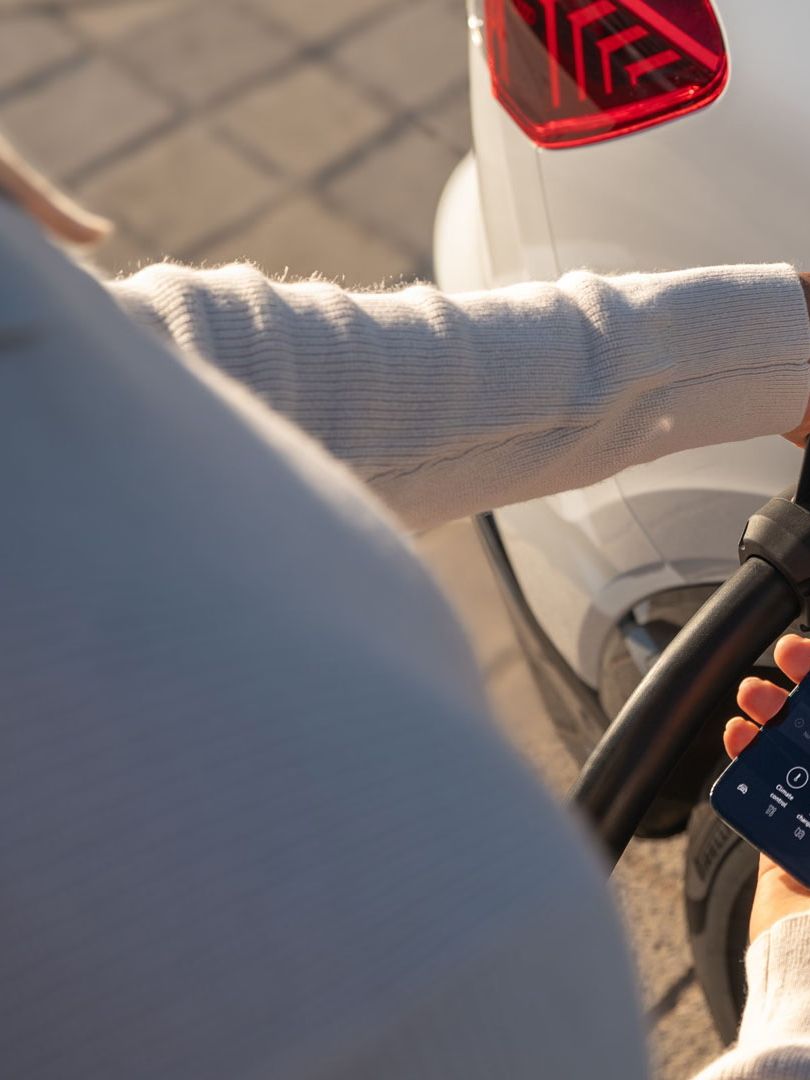 Osoba nabíja elektromobil pri nabíjacej stanici a sleduje priebeh nabíjania prostredníctvom aplikácie MyAudi.