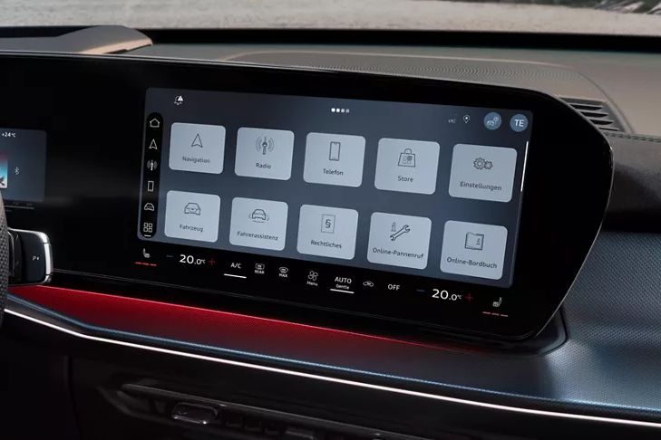 Obrázok zobrazuje interiér Audi Q3 Sportback a veľký displej na stredovej konzole. Na displeji sú viditeľné rôzne ovládacie možnosti pre navigáciu, rádio, integráciu smartfónu a funkcie vozidla. Vľavo od displeja je čiastočne viditeľný volant.