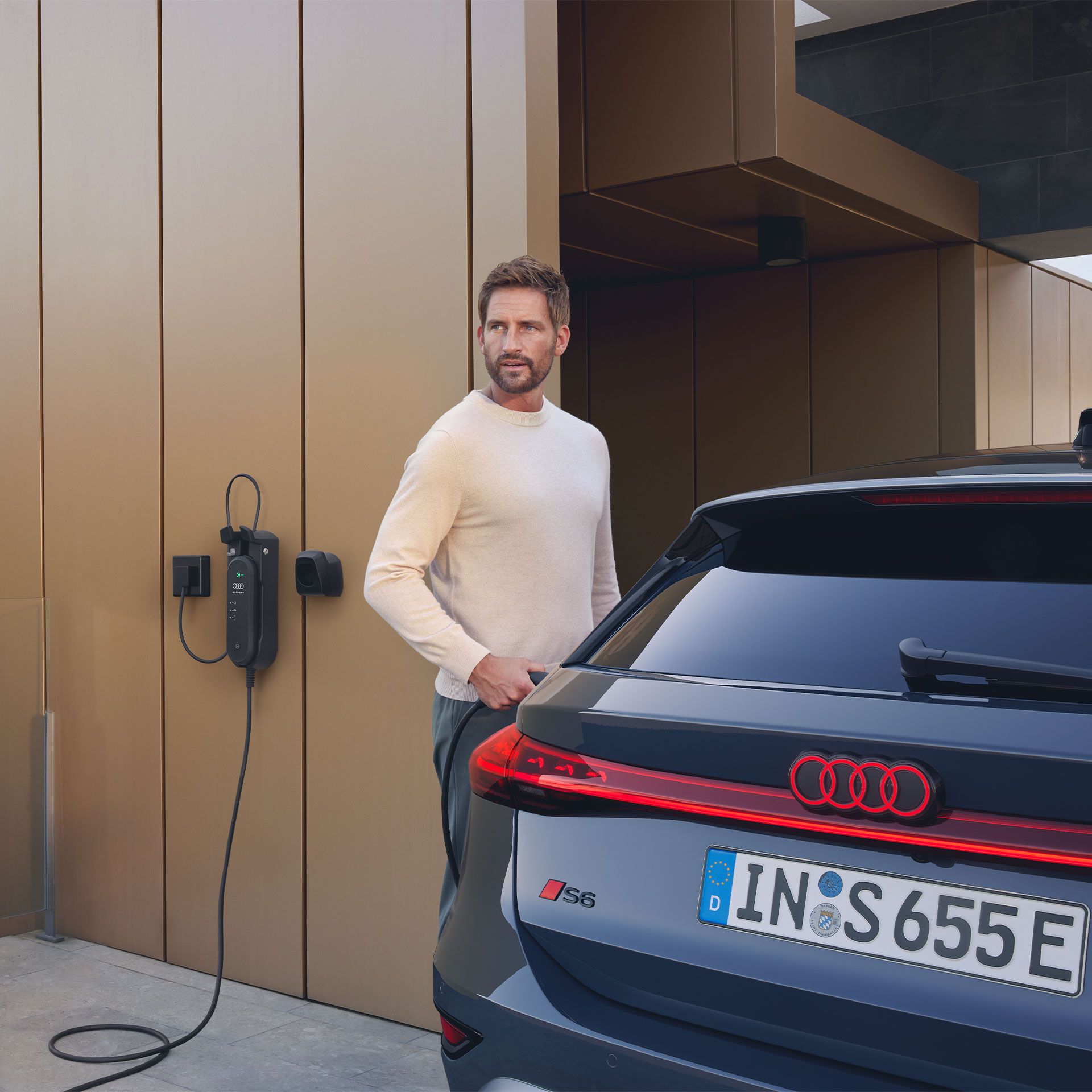 Muž stojí s nabíjacím káblom vedľa vozidla Audi S6 Avant e-tron