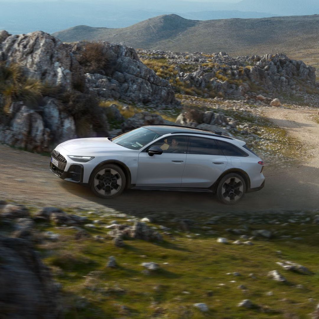 Audi A6 allroad e-hybrid prechádza po strmej štrkovej ceste v skalnatom prostredí.