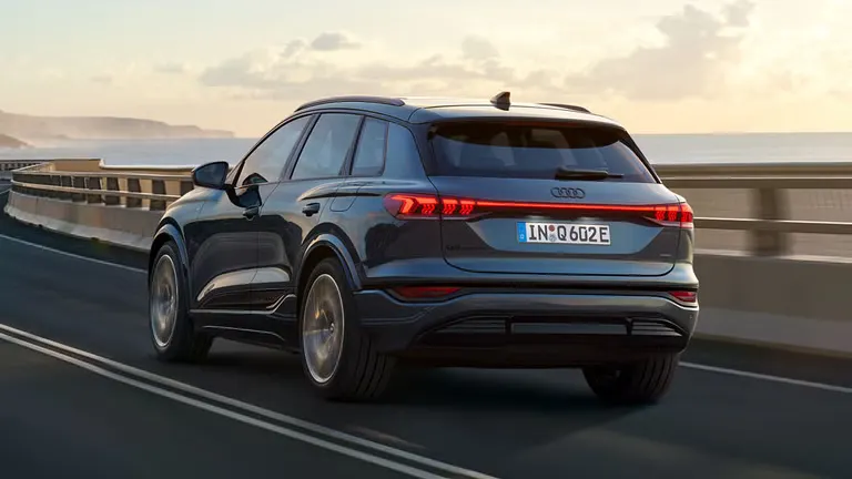 Audi Q6 SUV e-tron, ktoré jazdí po kľukatej ceste pri mori. V pozadí sú vidieť hory.