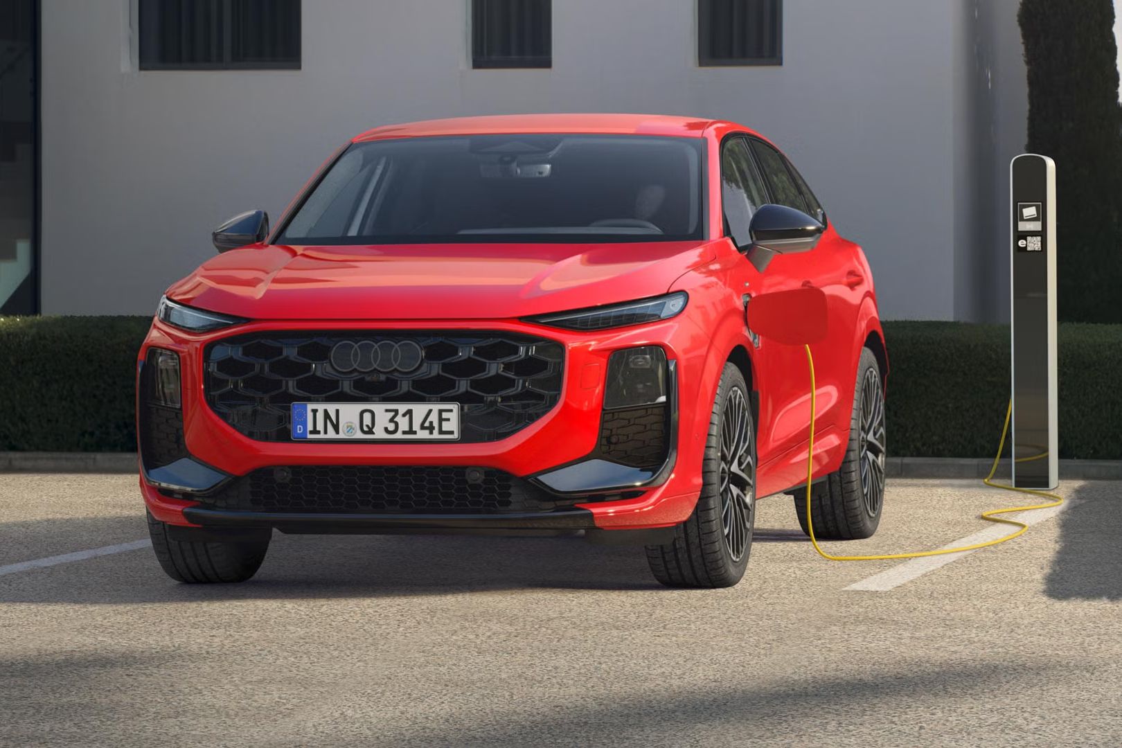 Červený Q3 Sportback e-hybrid je zaparkovaný pred nabíjacou stanicou a dobíja sa elektrickou energiou.