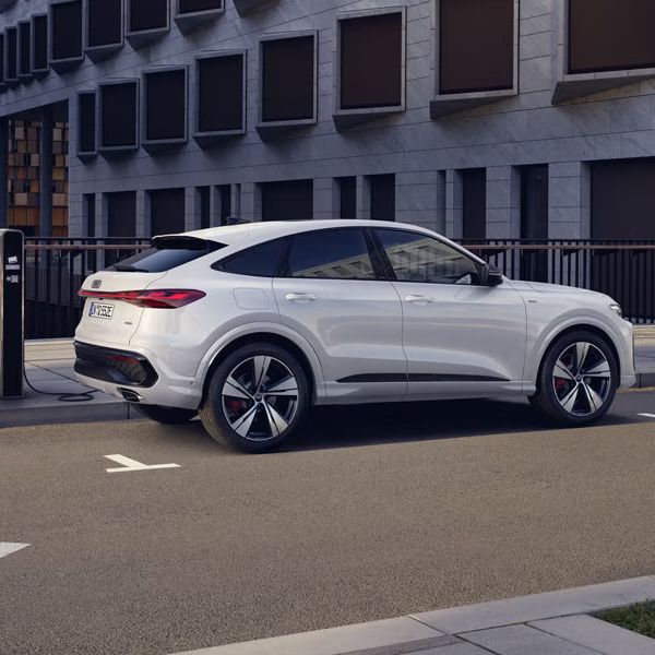 Biele Audi Q5 Sportback e-hybrid z bočného pohľadu, zaparkované pri chodníku a napojené na verejnú nabíjaciu stanicu.