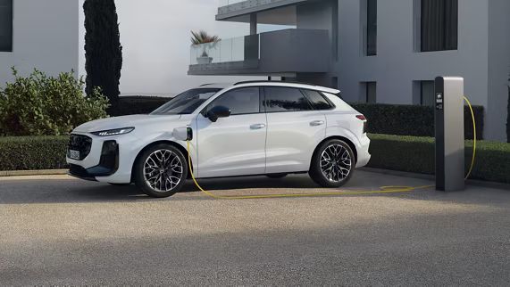 Audi Q3 Sportback e-hybrid zaparkované pred moderným bytovým domom pri nabíjacej stanici. Vozidlo sa nabíja.