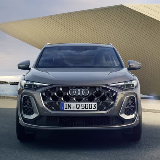 Pohľad na Audi Q5 SUV spredu zaparkovaný pred žltou modernou budovou na pobreží.