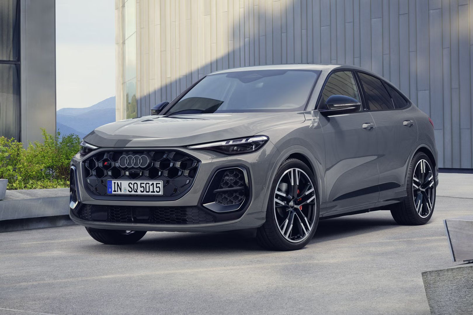 Audi SQ5 Sportback stojí pred veľkou budovou. Vozidlo je lakované v sivom odtieni Nardo.